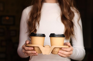 Woman holding paper coffee cups indoors, closeup