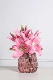 Beautiful pink lily flowers in vase on wooden table against white wall