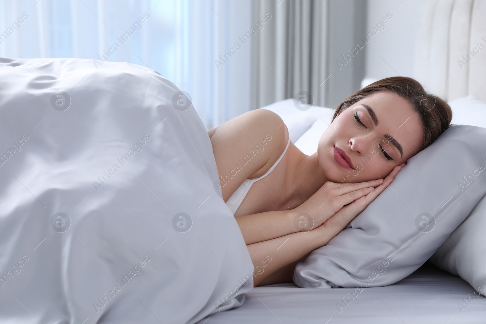 Photo of Young woman sleeping in comfortable bed with silky linens