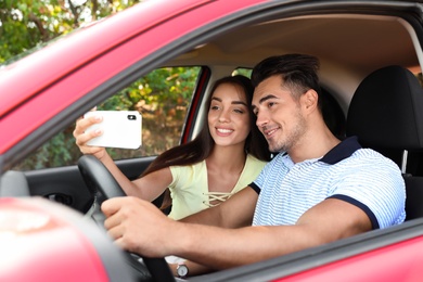 Happy young couple taking selfie in car on road trip