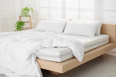 Photo of Wooden bed with soft white mattress, blanket and pillows in cozy room interior