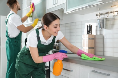 Photo of Portrait of woman cleaning table with rag and her colleague in kitchen