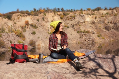 Photo of Female camper reading book while sitting on sleeping bag in wilderness