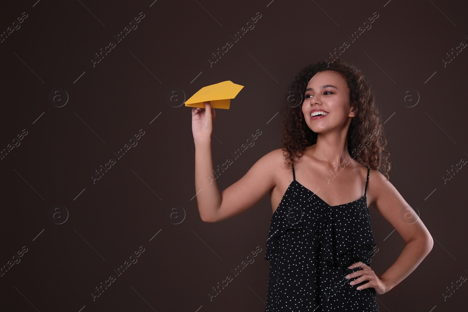 Photo of Beautiful African-American woman playing with paper plane on brown background. Space for text