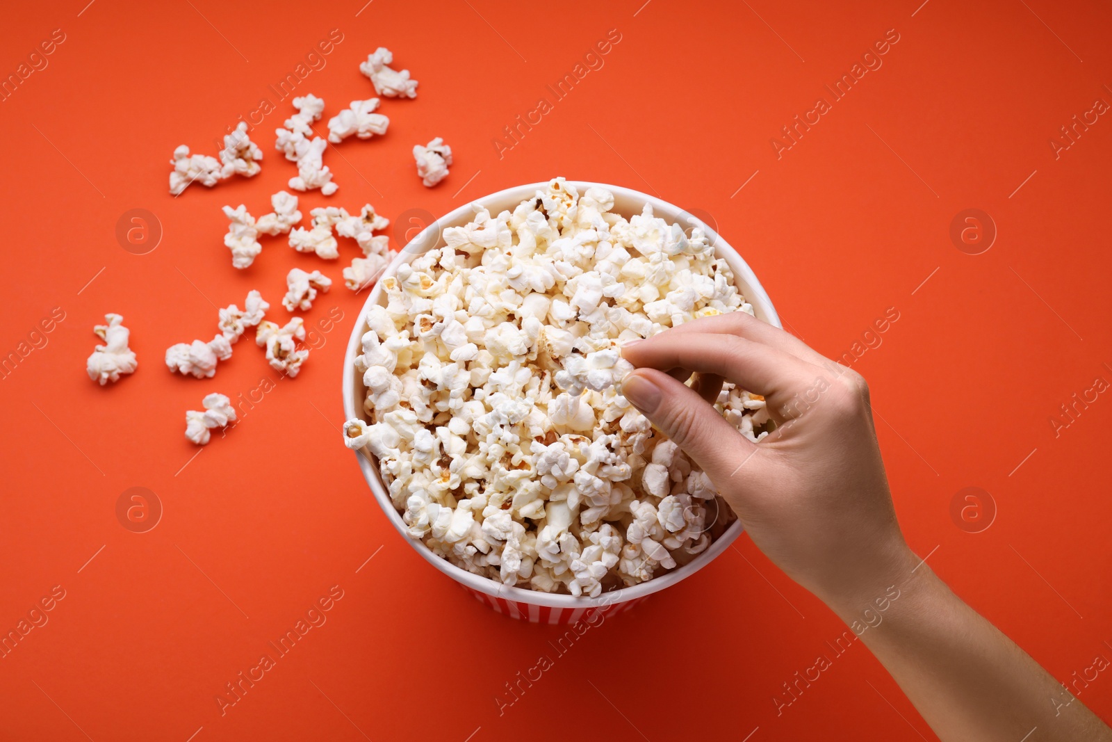 Photo of Woman taking fresh popcorn from bucket on orange background, above view