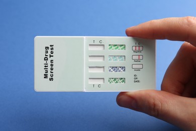 Woman holding multi-drug screen test on blue background, closeup