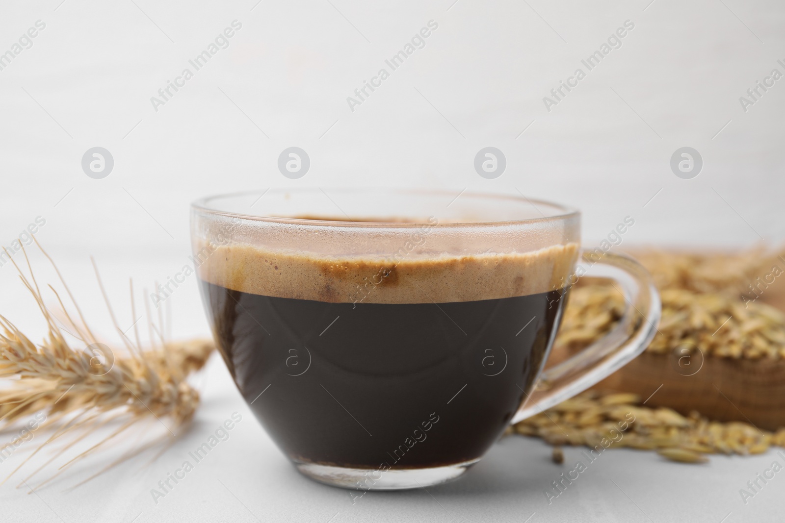 Photo of Cup of barley coffee and spike on white table, closeup