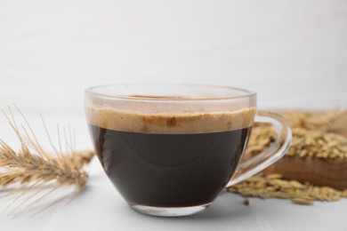 Cup of barley coffee and spike on white table, closeup