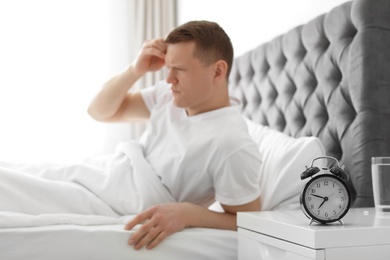 Photo of Alarm clock on nightstand of young man suffering from headache