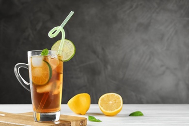 Photo of Cup of refreshing iced tea on white wooden table against grey background. Space for text