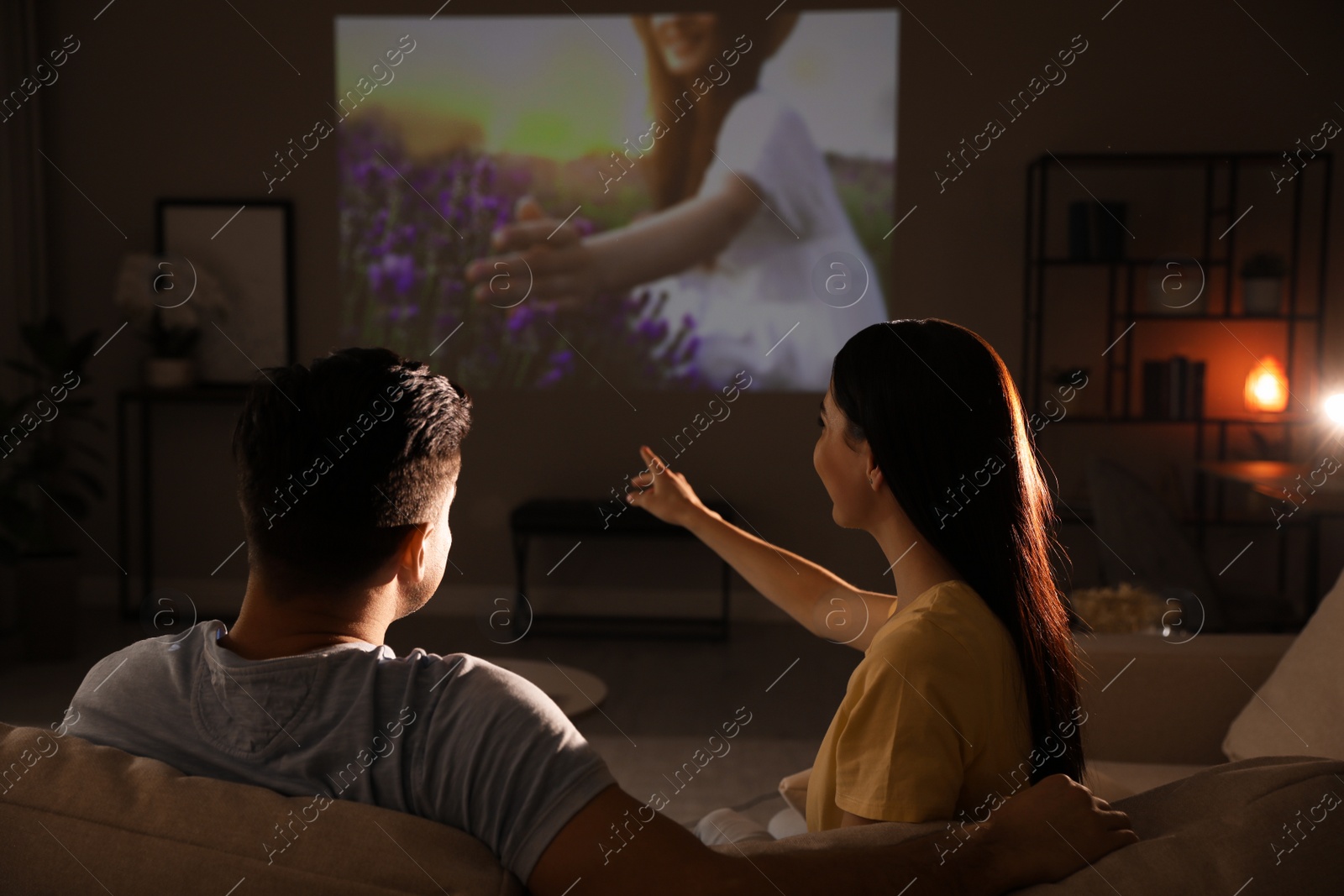 Photo of Couple watching movie on sofa at night, back view