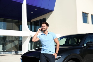 Young man talking on phone near modern car, outdoors