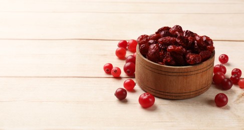 Photo of Dried cranberries in bowl and fresh berries on wooden table, space for text