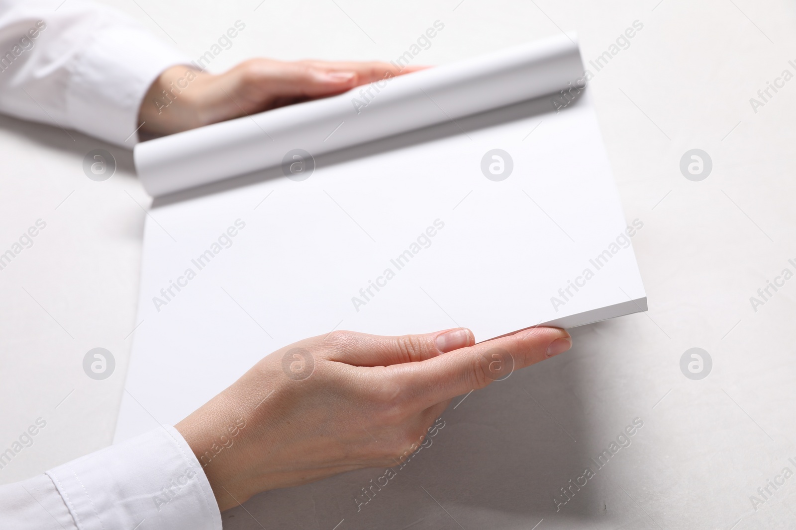 Photo of Woman holding notebook with blank pages at white table, closeup. Mockup for design