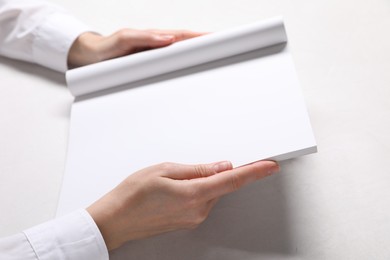 Photo of Woman holding notebook with blank pages at white table, closeup. Mockup for design