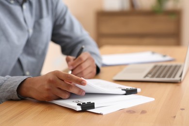 Man working with documents at wooden table in office, closeup