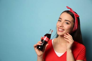MYKOLAIV, UKRAINE - JANUARY 27, 2021: Young woman holding bottle of Coca-Cola on light blue background. Space for text
