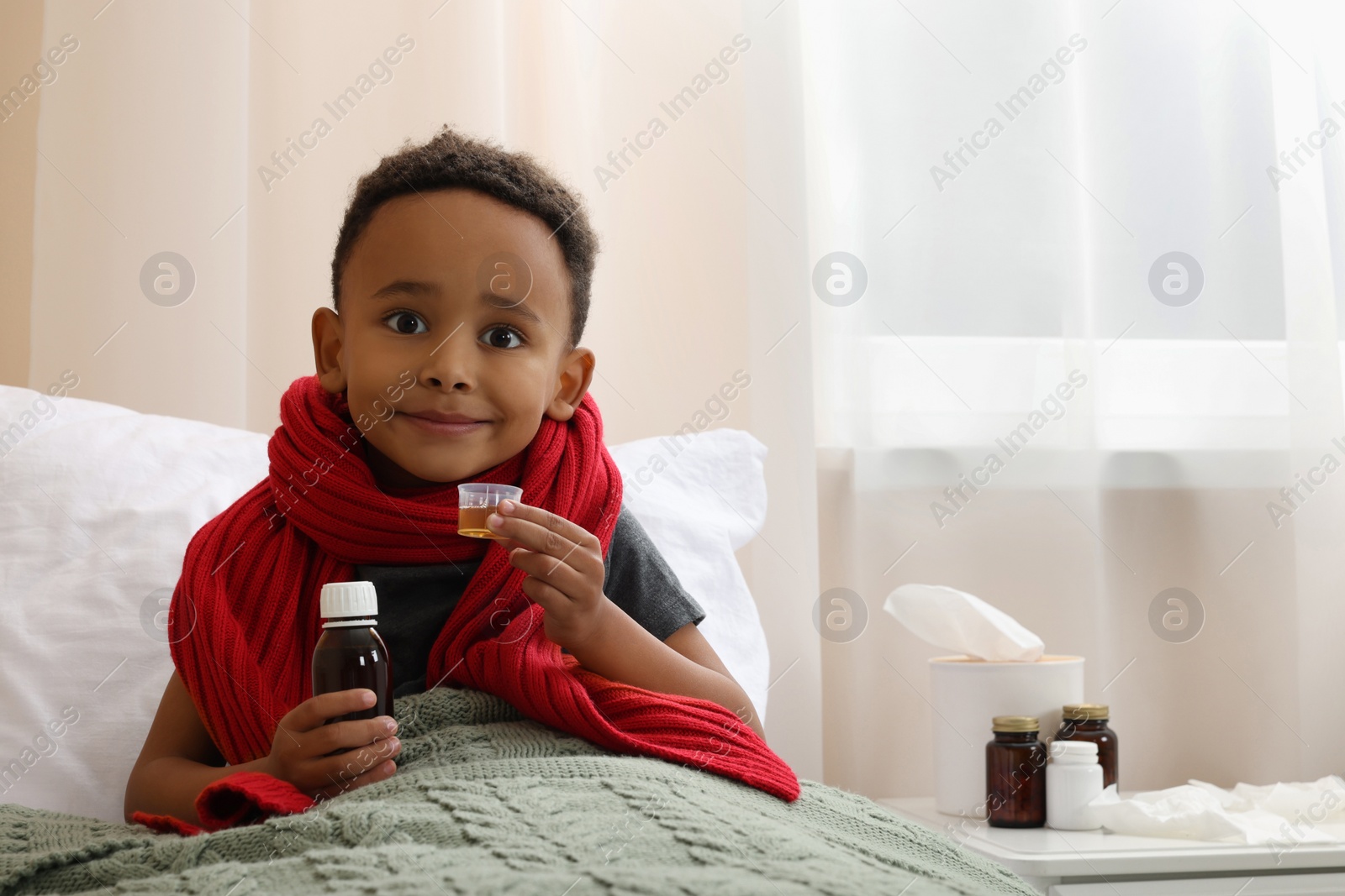 Photo of African-American boy taking cough syrup on bed at home, space for text. Cold medicine