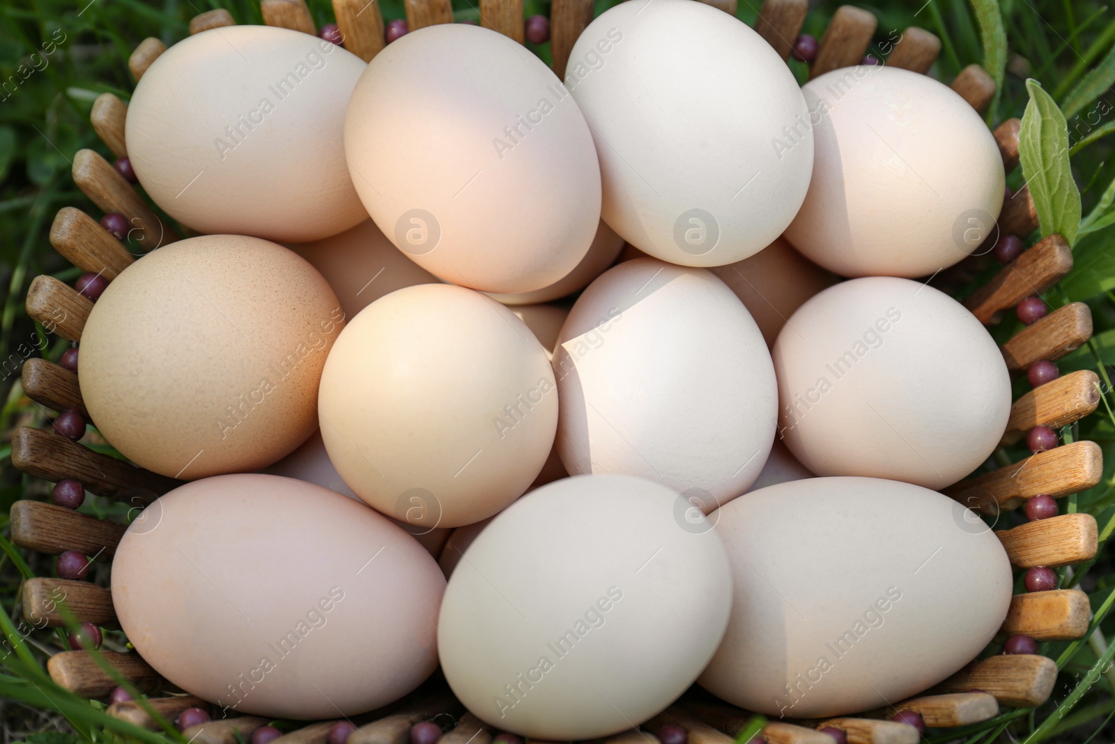 Photo of Fresh raw eggs in wooden basket on green grass, top view