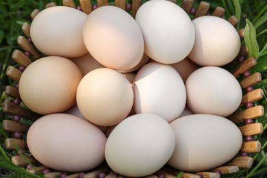 Photo of Fresh raw eggs in wooden basket on green grass, top view