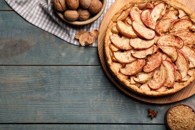 Photo of Delicious apple pie, sugar and walnuts on light blue wooden table, flat lay. Space for text