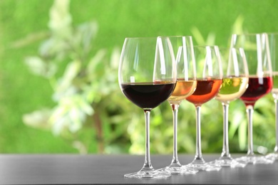Photo of Row of glasses with different wines on grey table against blurred background. Space for text
