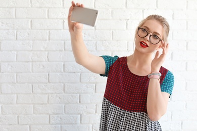 Attractive young woman taking selfie near brick wall