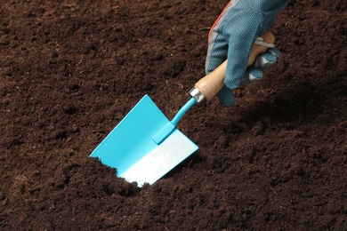 Photo of Woman digging soil with metal gardening trowel, closeup