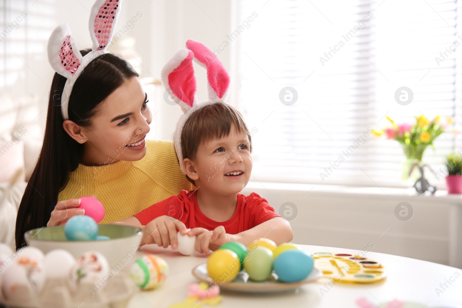 Photo of Happy mother with her cute son painting Easter eggs at table indoors