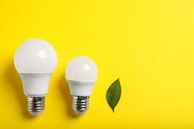 Photo of Light bulbs and green leaf on yellow background, flat lay. Space for text