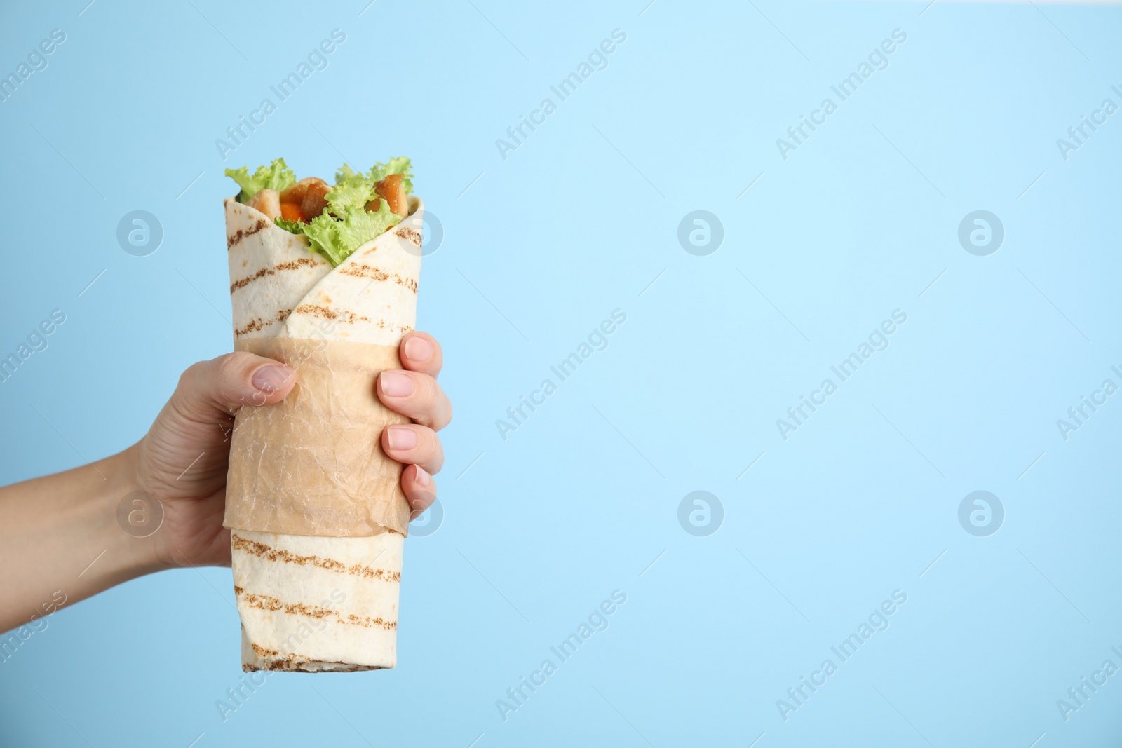 Photo of Woman holding delicious chicken shawarma on light blue background, closeup. Space for text