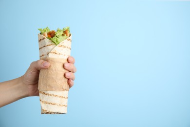 Photo of Woman holding delicious chicken shawarma on light blue background, closeup. Space for text