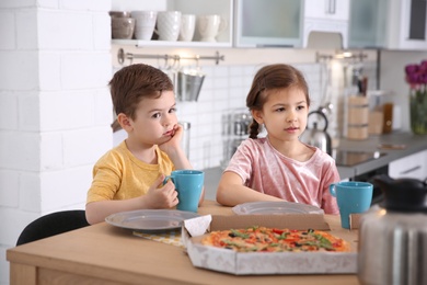 Photo of Cute little kids eating tasty pizza at home