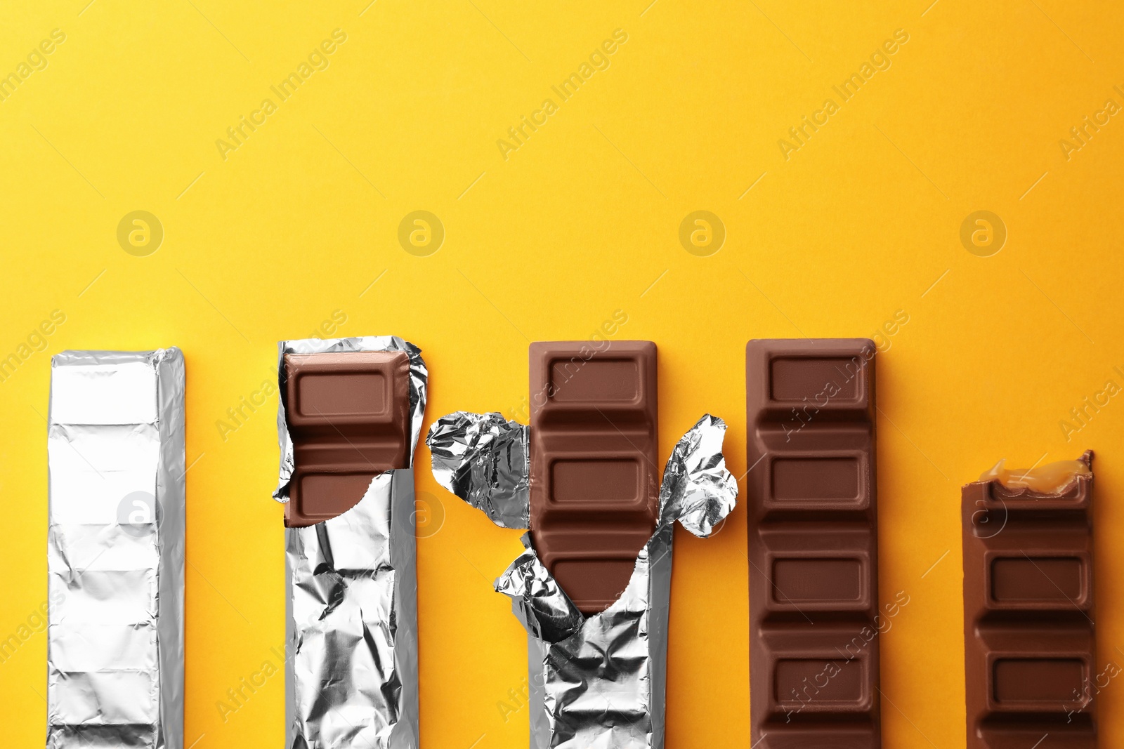 Photo of Tasty chocolate bars on yellow background, flat lay. Space for text