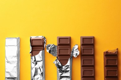 Tasty chocolate bars on yellow background, flat lay. Space for text