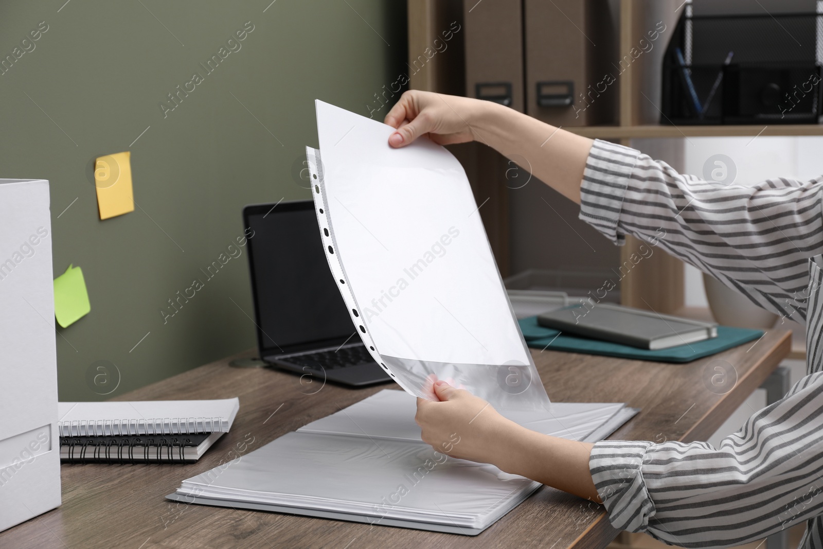 Photo of Woman putting paper sheet into punched pocket at wooden table, closeup