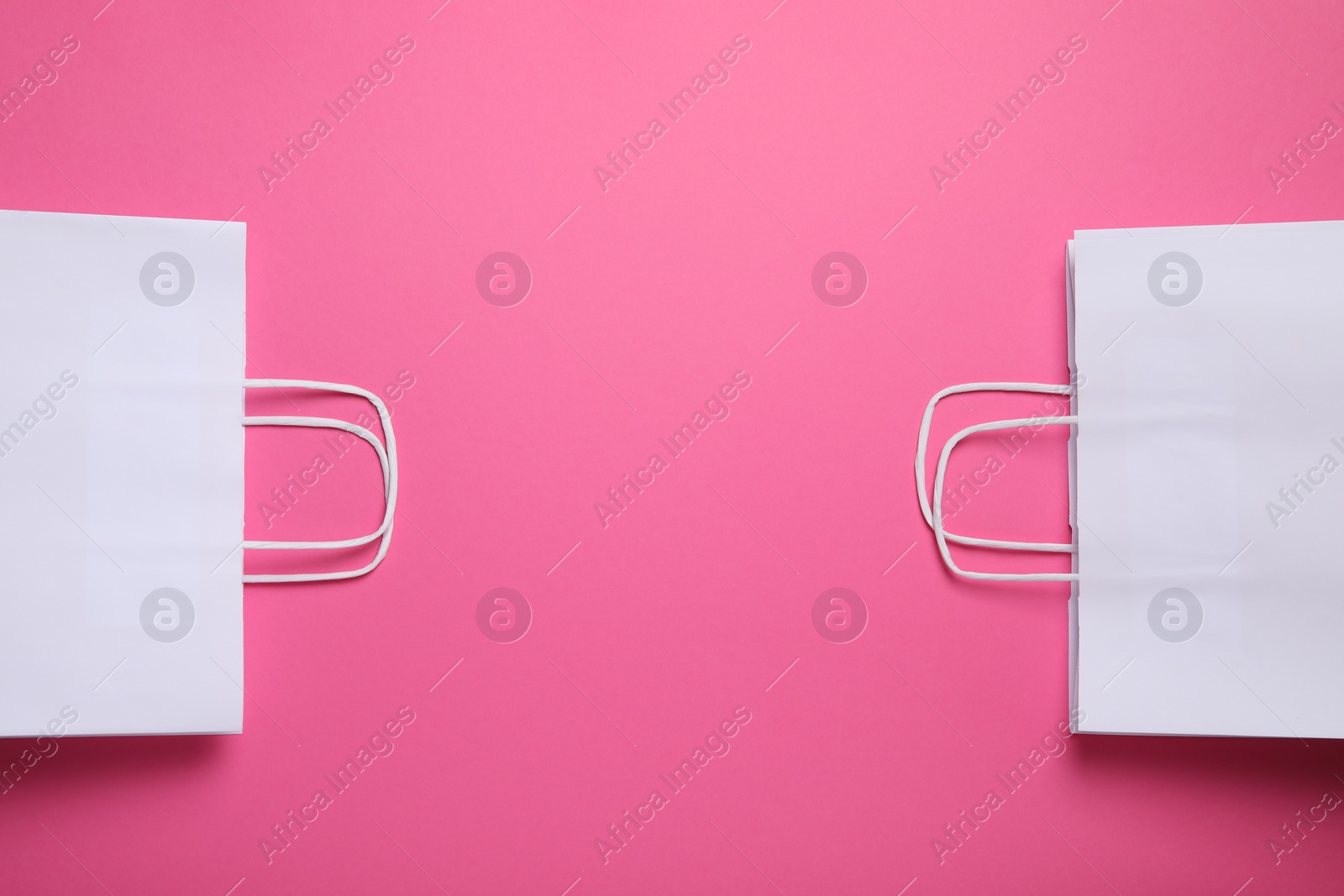 Photo of White paper bags on bright pink background, top view. Space for text