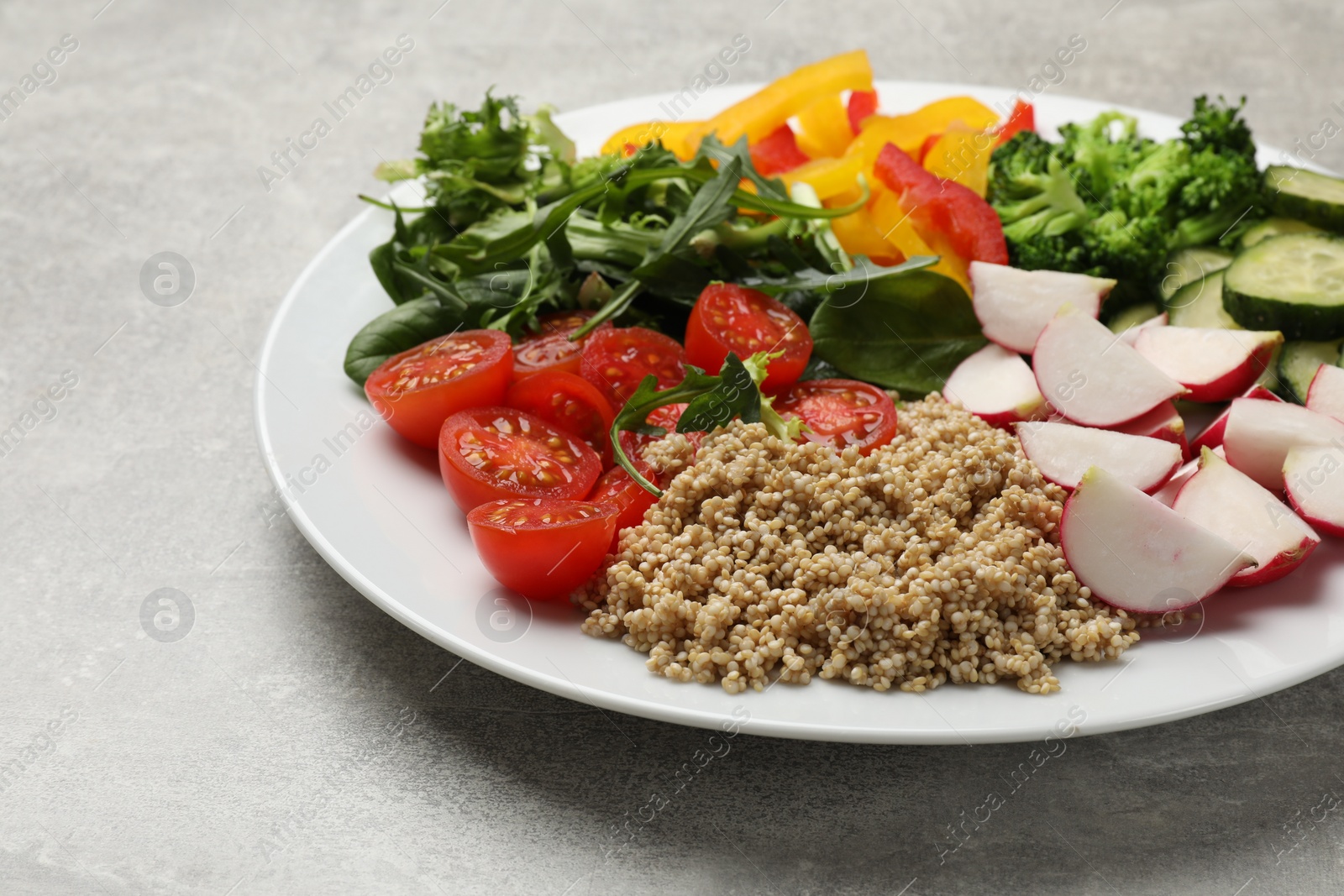 Photo of Vegetarian diet. Plate with tasty vegetables and quinoa on light grey table, closeup