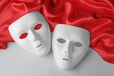 Photo of White theatre masks and red fabric on grey background, flat lay