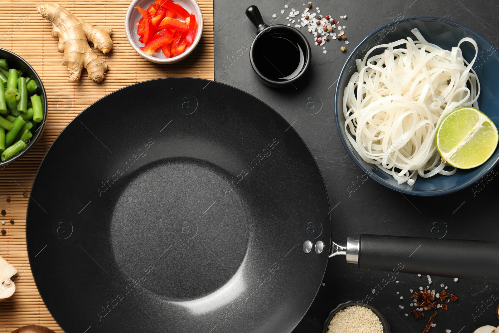 Photo of Flat lay composition with black wok, spices and products on dark table