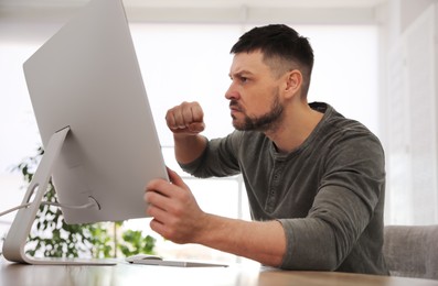 Photo of Emotional man in front of computer at workplace. Online hate concept