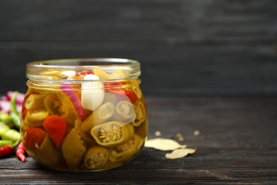 Photo of Glass jar with pickled peppers on wooden table. Space for text