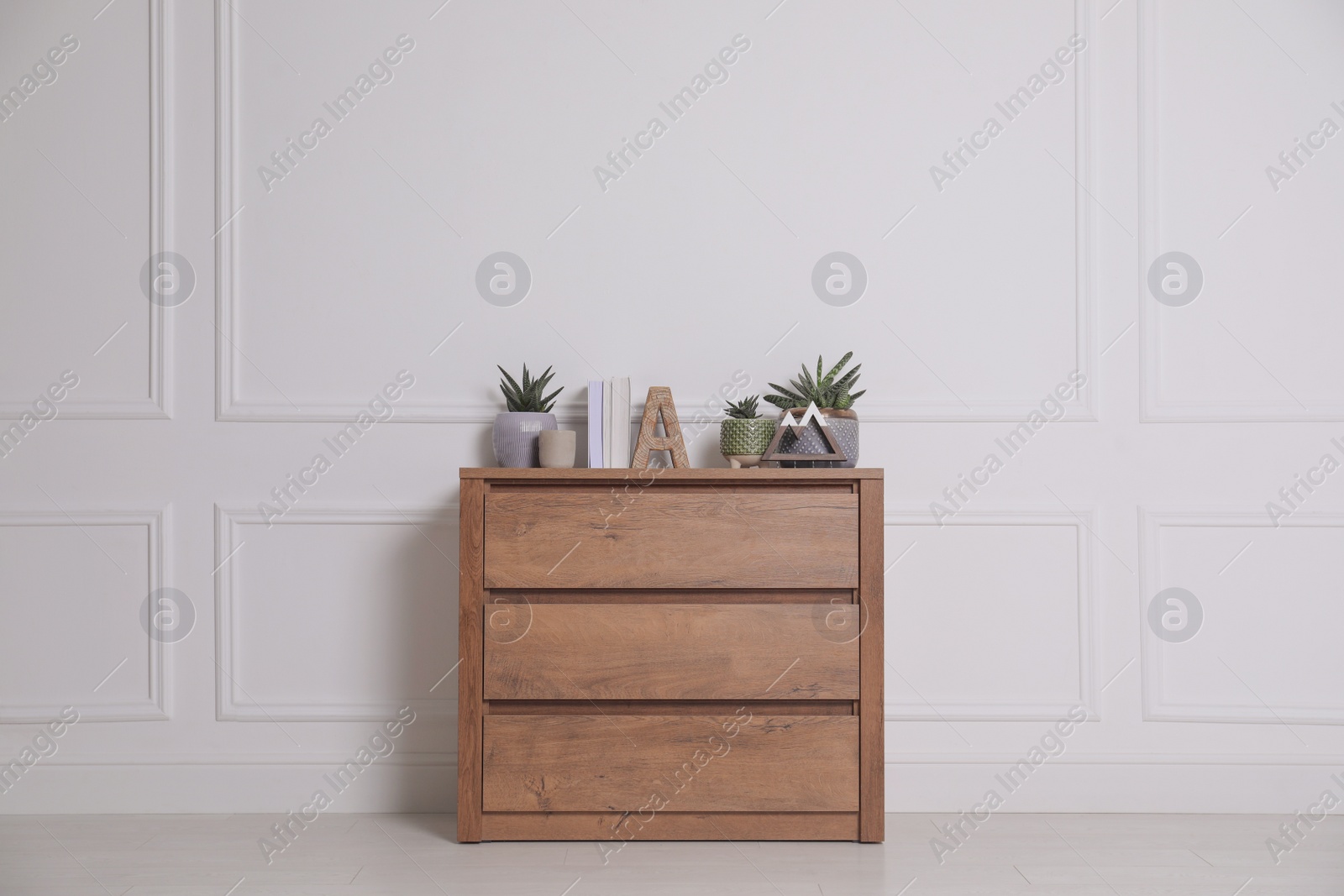 Photo of Books and beautiful plants on wooden chest of drawers near white wall indoors