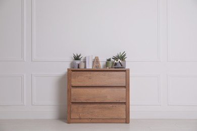 Photo of Books and beautiful plants on wooden chest of drawers near white wall indoors