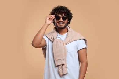 Photo of Handsome young smiling man in sunglasses on beige background