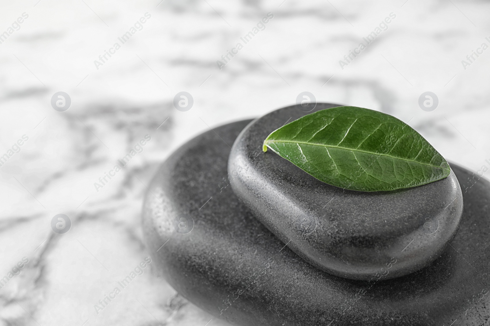 Photo of Spa stones and green leaf on marble table, space for text