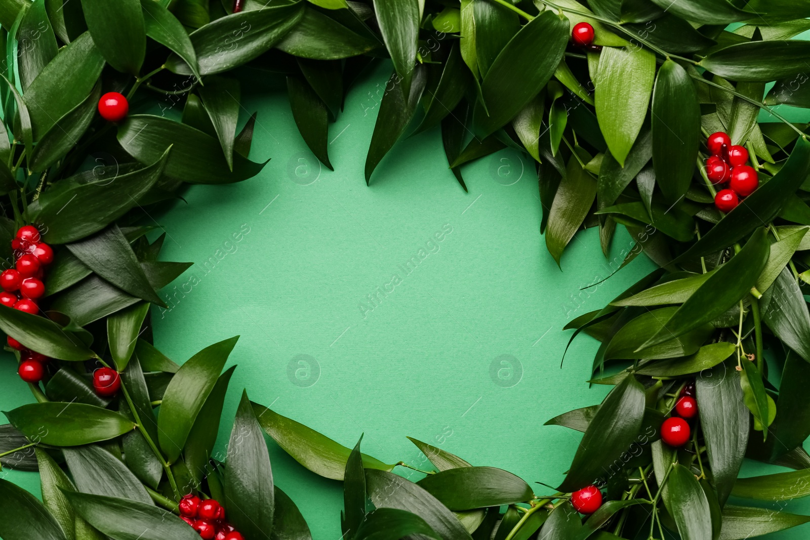 Photo of Beautiful handmade mistletoe wreath on green background, top view. Space for text