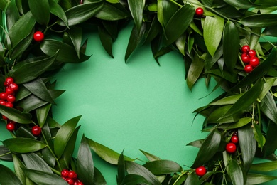 Beautiful handmade mistletoe wreath on green background, top view. Space for text