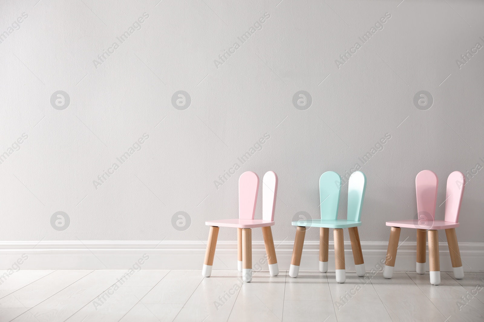 Photo of Cute little chairs with bunny ears near white wall indoors, space for text. Children's room interior