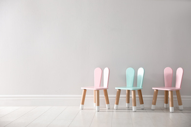 Photo of Cute little chairs with bunny ears near white wall indoors, space for text. Children's room interior